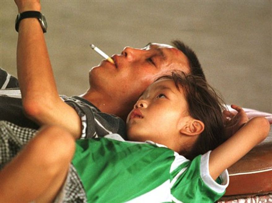 A Chinese man smokes a cigarette while reading to his daughter in Beijing, Aug. 25, 1997. (Associated Press) ** FILE **