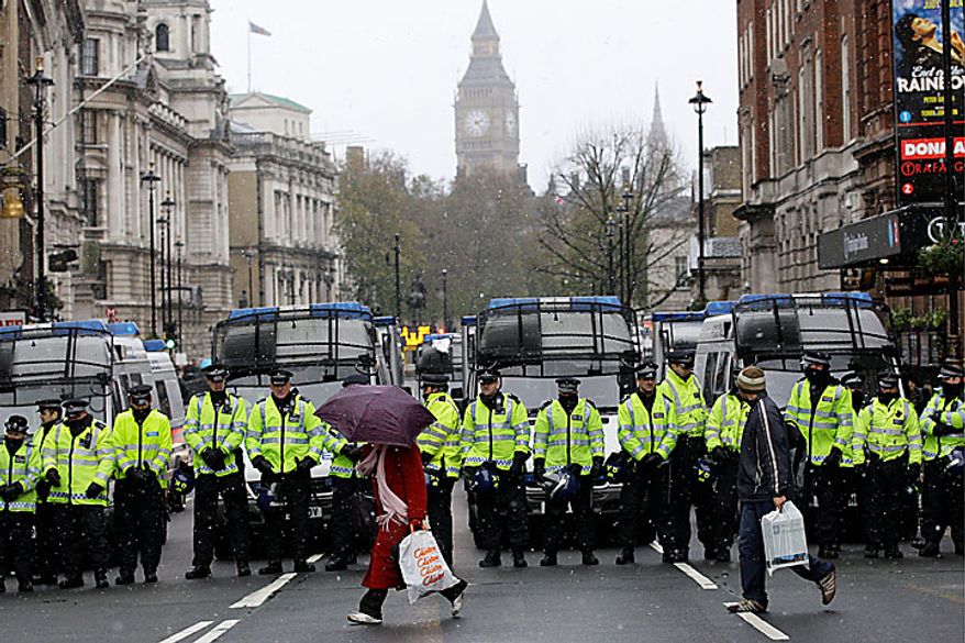 People walk past British police officers blocking off Whitehall leading to the Houses of Parliament in London as students march through the streets in a protest against tuition fees, Tuesday, Nov. 30, 2010. (AP Photo/Sang Tan)