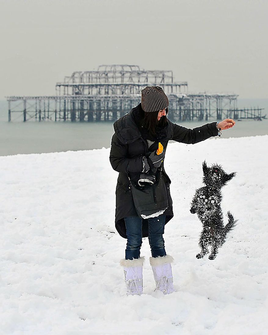 A woman plays with her dog on snow covered Brighton beach, England, Thursday Dec. 2, 2010. More heavy snow caused havoc across Britain on Thursday, keeping Gatwick airport closed for a second day, disrupting rail services and leaving travellers stranded. Commuters struggled to get to work as Britain's worst early winter weather in almost two decades showed no sign of easing its icy grip. (AP Photo/Clive Gee/PA)