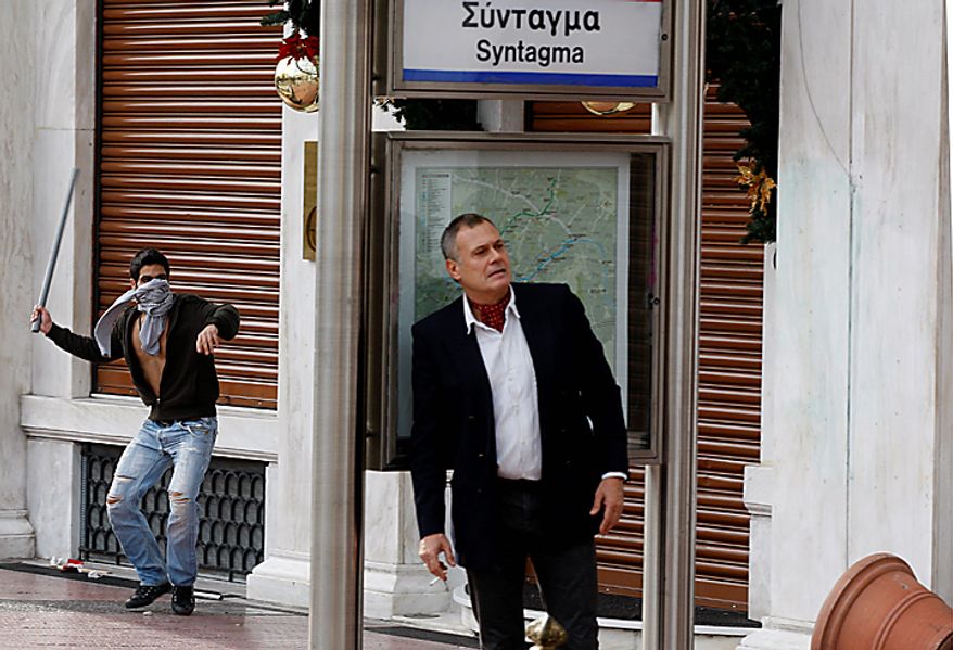 A youth prepares to throw a pole at riot police, not seen, as a man covers behind a Metro sign during a rally in Athens on Monday, Dec. 6, 2010. Youths hurled rocks and oranges at a government building in central Athens during a student protest to mark two years since the fatal police shooting of a teenage boy that sparked Greece's worst riots in decades. Police closed roads and deployed several thousand officers around the city but maintained a minimal presence at the site where some 1,500 students gathered outside Athens University's main buildings. (AP Photo/Thanassis Stavrakis)