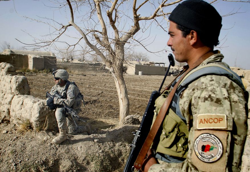 An Afghan soldier, right, stands as a U.S. soldier kneels on the ground in Panjwai district of Kandahar province, south of Kabul, Afghanistan Wednesday, Dec. 8, 2010. (AP Photo/Allauddin Khan)