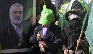 ** FILE ** Palestinian children, one masked and waving a green Islamic flag, sit near a photo of Gaza&#39;s Hamas prime minister, Ismail Haniyeh, during a rally to mark the 23rd anniversary of the group&#39;s founding, in Gaza City, Gaza Strip, on Tuesday, Dec. 14, 2010. (AP Photo/Majed Hamdan)