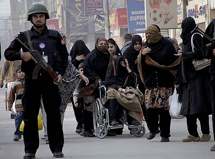 Police officer stands guard as Shi'ite Muslim women arrive to attend Muharram procession in Peshawar, Pakistan, on Thursday, Dec. 16, 2010. Muharram is observed around the world as ten days of mourning in remembrance of the martyrdom of Imam Hussein, the grandson of Prophet Muhammad. (AP Photo/Mohammad Sajjad)