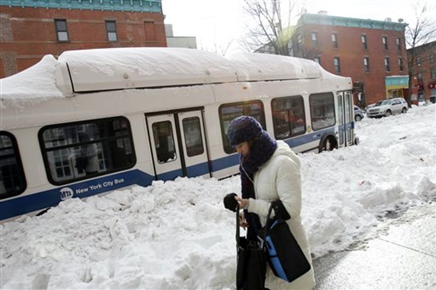 A woman walks past a New York City bus stuck in the snow in the Brooklyn borough of New York, Tuesday, Dec. 28, 2010. (AP Photo/Seth Wenig)