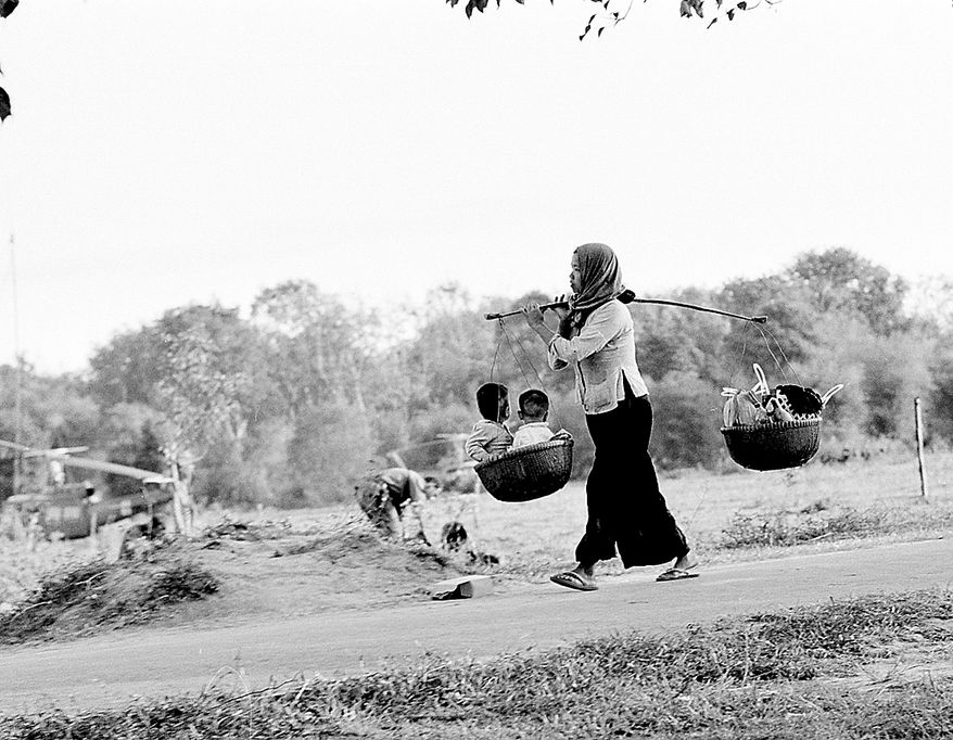 A Vietnamese mother carries her children in one of two baskets attached to a stick she holds over her shoulder in Ben Suc, Vietnam, Jan. 17, 1967 during the Vietnam War. Villagers of Ben Suc are leaving their homes to be resettled at a refugee camp in another area. They are part of the estimated 10,000 peasants expected to be evacuated from the Iron Triangle, Viet Cong stronghold, as U.S. troops push through. (AP Photo/Henri Huet)