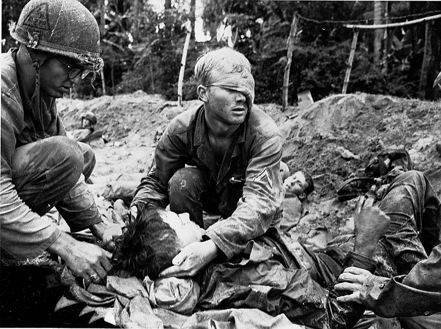 First Cavalry Division Medic Thomas Cole, from Richmond, Va., wearing a bandage over the left side of his face, tends to an unidentified soldier in a trench during battle in the Vietnam War, 1966. The trench had been the first line of Viet Cong and North Vietnamese defense until it was taken by American forces. (AP Photo/Henri Huet)