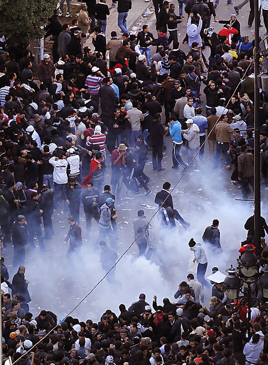Demonstrators runs as police throw teargas during a demonstration in Tunis, Friday, Jan. 14, 2011. Tunisia's president declared a state of emergency and announced that he would fire his government as violent protests escalated Friday, with gunfire echoing in the North African country's usually calm capital and police lobbing tear gas at protesters. (AP Photo/Christophe Ena)
