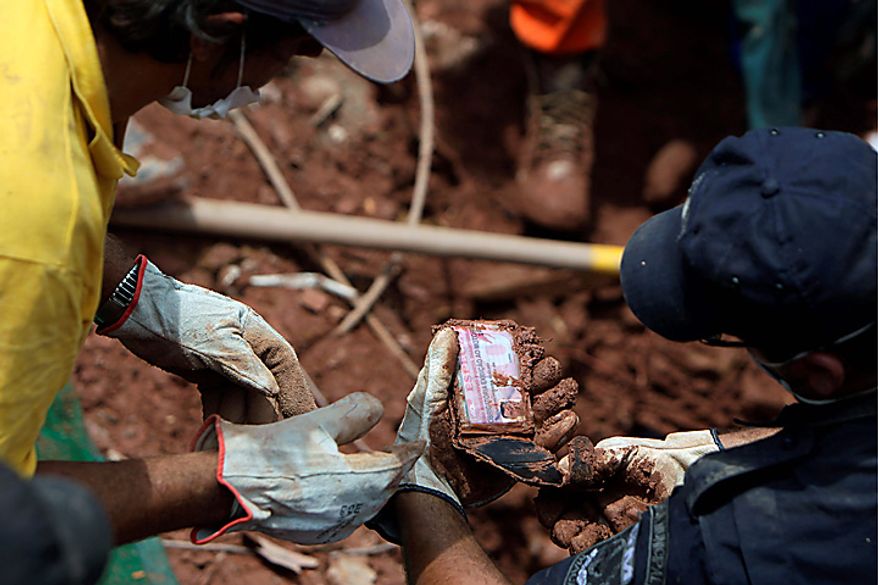 Rescue workers check the ID of Edilson da Silva found next to recovered bodies of landslides victims in Nova Friburgo, Brazil, Monday, Jan. 17, 2011. Brazil's army on Monday sent 700 soldiers to help throw a lifeline to desperate neighborhoods that have been cut off from food, water or help in recovering bodies since mudslides killed at least 642 people. (AP Photo/Felipe Dana)