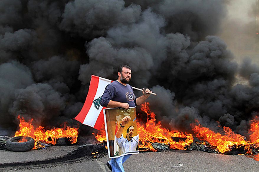 A protester carries a picture of outgoing Prime Minister Saad Hariri and a Lebanese flag as he walks in front of burning tires in the southern port city of Sidon, Lebanon, Tuesday, Jan. 25, 2011. Sunnis protested the rising power of the Shi'ite militant group Hezbollah on Tuesday, burning tires and torching a van belonging to Al Jazeera as Lebanese lawmakers gave the militant group's pick for prime minister enough support to form the next government. (AP Photo/Mohammed Zaatari)