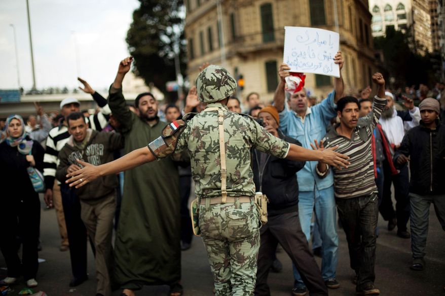 DEFIANT: Protesters march past an Egyptian soldier Sunday in Cairo as they move toward Tahrir Square during a sixth day of demonstrations against the government. (Associated Press)