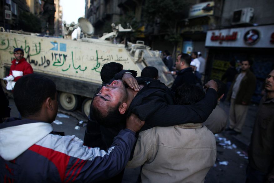 An injured anti-government protester is carried past an army vehicle during clashes Wednesday in Tahrir Square in Cairo. Protesters continue to call for President Hosni Mubarak's immediate ouster. (Associated Press)