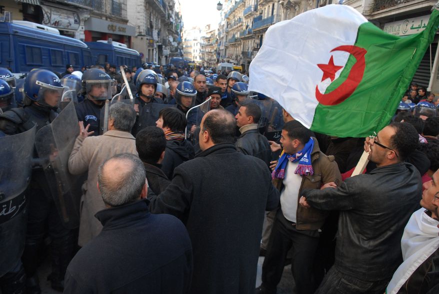 ** FILE ** Protesters carrying an Algerian flag face riot policemen In Algiers on Saturday, Jan. 22, 2011, during a demonstration against a ban on public gatherings. (AP Photo)