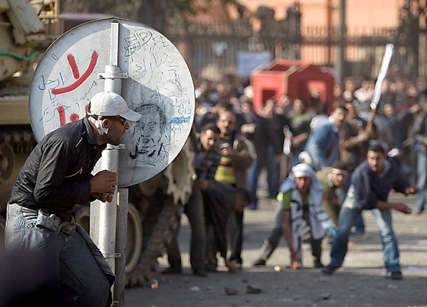 An anti-government protester shelters behind a road sign as pro-government demonstrators, background, throw rocks, in Cairo, Egypt, Wednesday, Feb.2, 2011. Several thousand supporters of President Hosni Mubarak, including some riding horses and camels and wielding whips, clashed with anti-government protesters as Egypt's upheaval took a dangerous new turn. In chaotic scenes, the two sides pelted each other with stones, and protesters dragged riders off their horses. (AP Photo/Sebastian Scheiner)