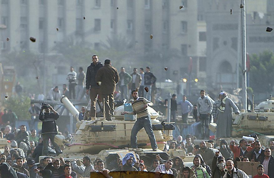 Stones fly through the air as supporters of President Hosni Mubarak, foreground , fight with anti-Mubarak protesters, rear, standing on army tanks in Cairo, Egypt, Wednesday, Feb.2, 2011. Several thousand supporters of Mr. Mubarak, including some riding horses and camels and wielding whips, clashed with anti-government protesters Wednesday as Egypt's upheaval took a dangerous new turn. (AP Photo/Ahmed Ali)