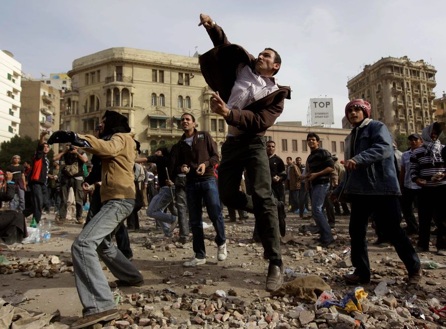 Anti-government protesters throw stones during clashes in Cairo on Thursday. Egypt's prime minister apologized for an attack by government supporters. (Associated Press)