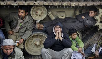 Anti-government protesters sit on and lie inside the tracks of an Egyptian army tank, both to prevent the tank from moving and to shield themselves from the rain, at a protest site opposite the Egyptian Museum near Tahrir Square in downtown Cairo on Sunday, Feb. 6, 2011. (AP Photo/Ben Curtis)
