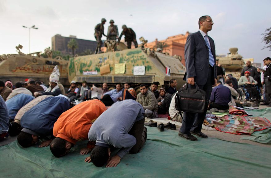 Anti-government protesters pray in front of an army armored vehicle as one stands to have his picture taken by a friend at the continuing protest in Tahrir Square in downtown Cairo. Egypt's embattled regime announced a 15 percent raise for government employees in an effort to defuse popular anger. (Associated Press)