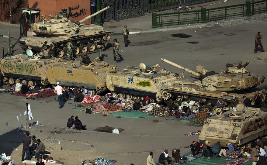 Anti-Mubarak protesters are seen next to Egyptian army tanks and armored vehicles near Tahrir Square in Cairo on Wednesday, Feb. 9, 2011. Protesters appear to have settled in for a long standoff, turning the square into a makeshift village with tens of thousands coming every day, with some sleeping in tents made of blankets and plastic sheeting. (AP Photo/Emilio Morenatti)