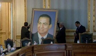 ** FILE ** Officials remove a painting of ousted Egyptian President Hosni Mubarak at the main Cabinet building in Cairo on Sunday, Feb. 13, 2011. Egyptians are removing portraits of Mr. Mubarak that have hung in public and private institutions throughout his three decades in power. (Associated Press)