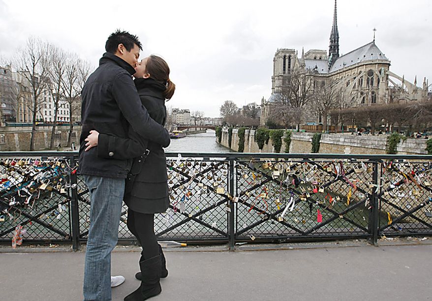 French lovers David, 22, and Charlene, 23, share a Valentine's Day kiss near Notre-Dame Cathedral in Paris on Monday, Feb. 14, 2011. The padlocks on the fence of the bridge belong to lovers who throw the keys to the locks into the Seine as a symbol of enduring love. (AP Photo/Jacques Brinon )
