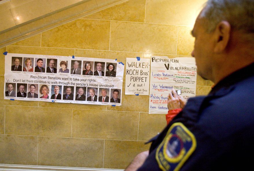 Police officer Greg Friberg of Milwaukee looks a poster at the Capitol in Madison, Wis. Opponents of a bill to limit collective-bargaining rights protested for the sixth day. (Associated Press)