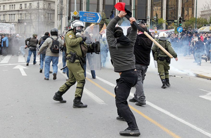 A protester hits a riot police officer with a stick during clashes in central Athens on Wednesday. Scores of youths hurled rocks and fire bombs at riot police after clashes broke out Wednesday during a mass rally taking place as part of a general strike. (Associated Press)