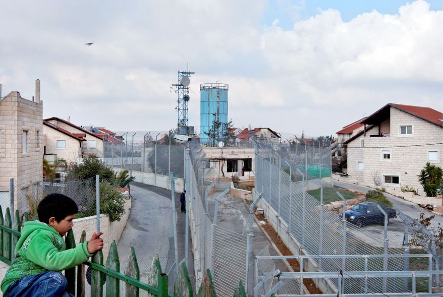 A Palestinian boy sits on a rooftop near the fenced-in house of al-Ghirayim family between the Jewish settlement of Givon Hahadasha and the West Bank village of Beit Ijza. The family's 10 members can only reach the house via a 40-yard passageway connecting them to the Arab village of Beit Ijza. (Associated Press)