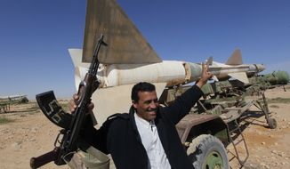 A Libyan popular defence committee member, holds his AK-47 as he flashes V sign in front an anti-aircraft missile at an abandoned Libyan military base near Tobruk, Libya, on Wednesday, Feb.23, 2011. Heavy gunfire broke out in Tripoli as forces loyal to Moammar Gadhafi tightened their grip on the Libyan capital while anti-government protesters claimed control of many cities elsewhere and top government officials and diplomats turn against the longtime leader. (AP Photo/Hussein Malla)