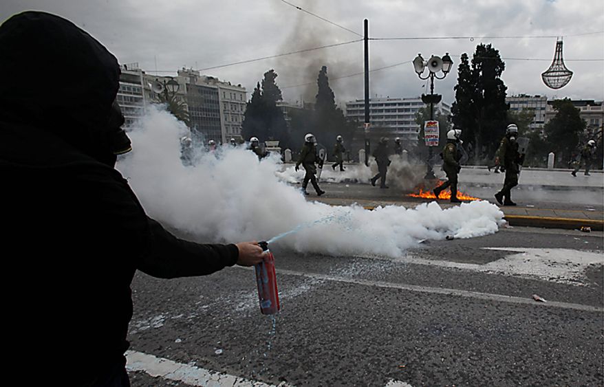 A protester uses a fire extinguisher as riot police pass beside tear gas during clashes in Athens on Wednesday, Feb. 23, 2011. Scores of youths hurled rocks and petrol bombs at riot police after the clashes broke out during a mass rally taking place as part of a general strike. (AP Photo/Kostas Tsironis)