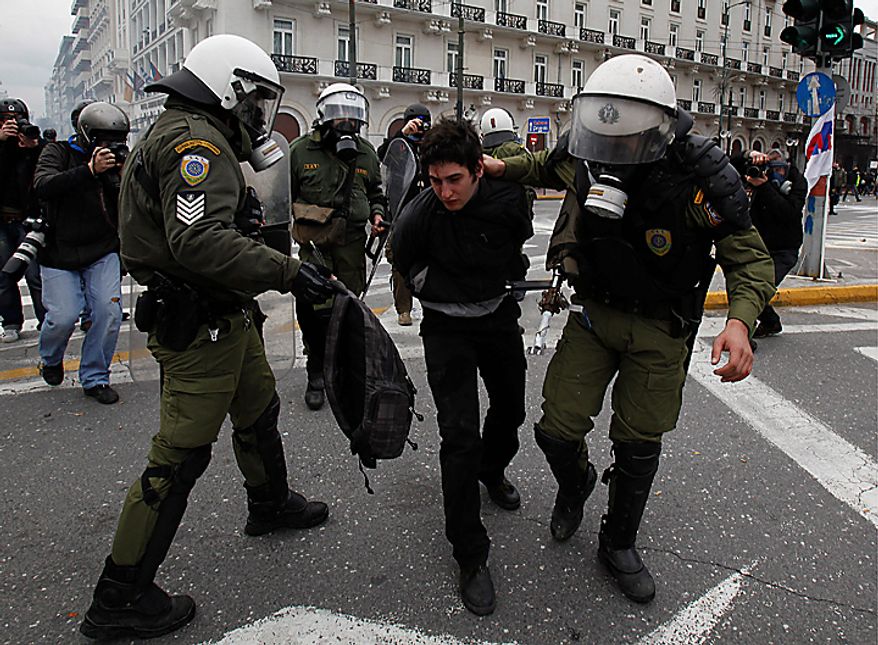 A riot policeman (right) detains a protester while another (left) holds a bag from which an arrow protrudes during clashes in Athens on Wednesday, Feb. 23, 2011. Scores of youths hurled rocks and gasoline bombs at riot police after clashes broke out during a mass rally taking place as part of a general strike. (AP Photo/Kostas Tsironis)