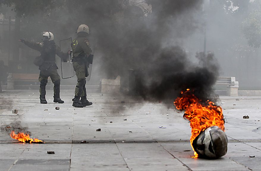 A police helmet is on fire in front of riot policemen in Syntagma Square in central Athens during clashes on Wednesday, Feb. 23, 2011. Scores of youths hurled rocks and gasoline bombs at riot police after the clashes broke out during a mass rally taking place as part of a general strike. (AP Photo/Petros Giannakouris)