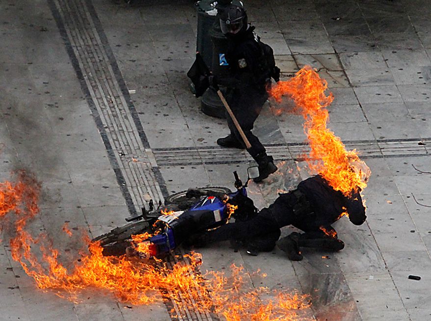 A motorcycle policeman burns as his colleague tries to help him after protesters throw a gasoline bomb in Athens on Wednesday, Feb. 23, 2011. Scores of youths hurled rocks and Molotov cocktails at riot police after clashes broke out during a mass rally taking place as part of a general strike. (AP Photo/Dimitri Messinis)