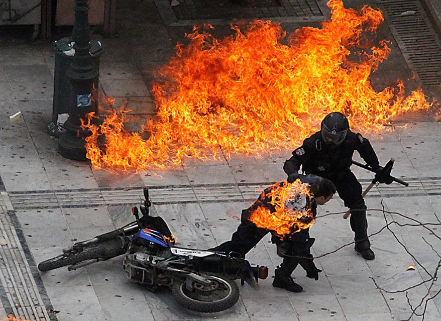 A motorcycle policeman burns as his colleague tries to help him after protesters threw a gasoline bomb in Athens on Wednesday, Feb. 23, 2011. Scores of youths hurled rocks and Molotov cocktails at riot police after clashes broke out during a mass rally that was part of a general strike. (AP Photo/Dimitri Messinis)