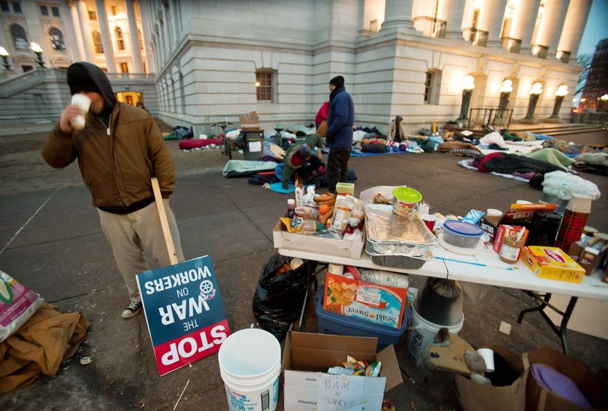 A man drinks coffee outside of the state Capitol on Thursday in Madison, Wis., as campers wake up after spending the night. Demonstrators are in their 16th day of protests. (Associated Press)