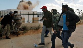 Rebels run as smoke rises from a house hit during an airstrike Tuesday in the oil port of Ras Lanouf in eastern Libya. Warplanes kept up attacks to prevent the opposition from advancing toward leader Col. Moammar Gadhafi&#39;s stronghold in the capital of Tripoli. (Associated Press)