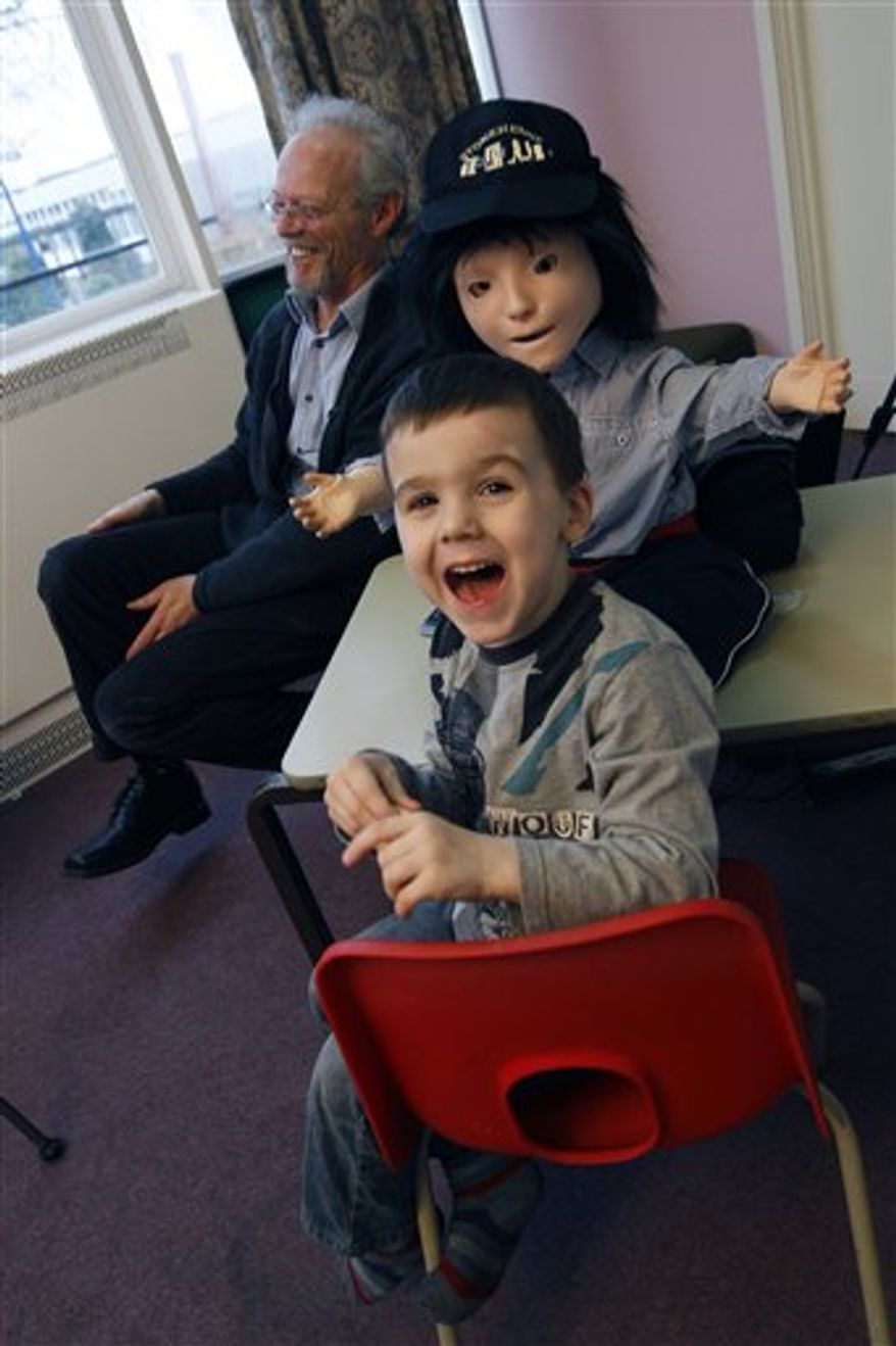 In this Monday, Feb. 28, 2011 photo, Dr Ben Robins, right, a research fellow at Hertfordshire University shows off two 'Kasper' robots that he hopes will help with autistic children, in Hatfield, England. Autistic children play with the robot for up to 10 minutes alongside a scientist who controls the robot with a remote control. The robot, named Kaspar, is programmed to do things like smile, frown, laugh, blink and wave his arms. He has shaggy black hair, a baseball cap, a few wires protruding from his neck, and striped red socks. He was built by scientists at the University of Hertfordshire at a cost of about 1,300 pounds ($2,118). (AP Photo/Alastair Grant)