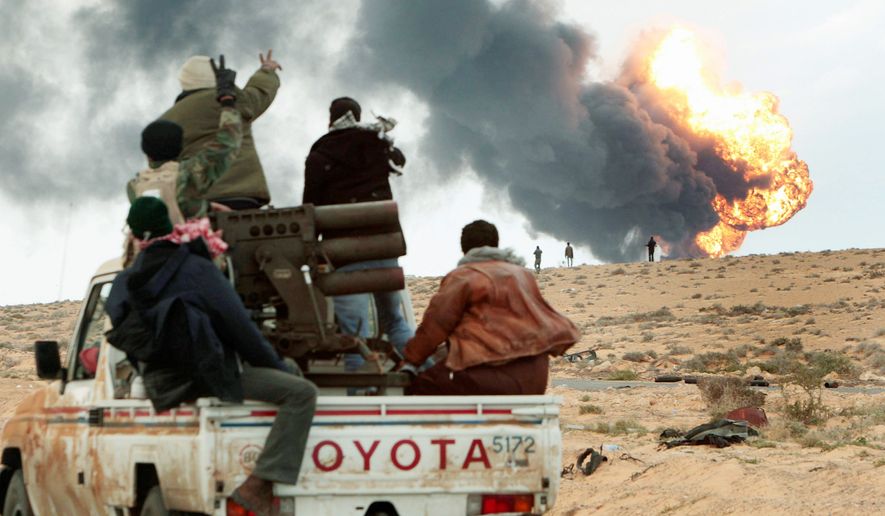 AFLAME: Anti-Gadhafi rebels transport a multiple-rocket launcher Wednesday as flames rise from a fuel-storage facility that was attacked in fighting with pro-Gadhafi forces, in Sedra, Libya. (Associated Press)