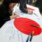 Rina Hirano (left), a Japanese Embassy worker, and Ian Rinehart, a George Washington University graduate student, write messages of support on Japanese flags at the fundraiser Sunday at Cafe Asia in Arlington. (Barbara L. Salisbury/The Washington Times)