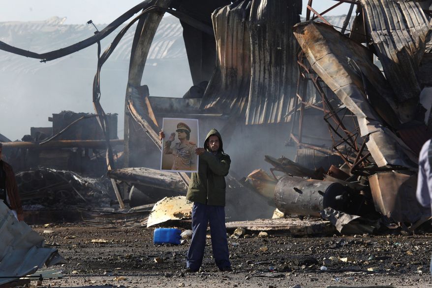 A supporter of Col. Moammar Gadhafi displays the Libyan leader's portrait Tuesday amid the wreckage of a Tripoli naval base warehouse hit by missiles Monday. (Associated Press)