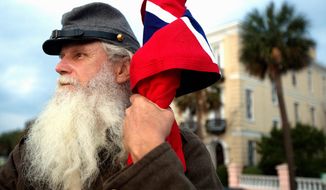 ** File ** At a Civil War reenactment event, a man holds a Confederate naval jack flag as he looks toward Fort Sumter from the Battery in downtown Charleston, S.C., on April 12, 2011, to mark the 150th anniversary of the start of the Civil War. (Associated Press)