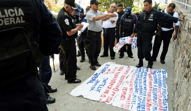 Police examine a &quot;narco-manta,&quot; a warning message painted on a banner left near the site where five dismembered bodies were found on the sidewalk next to a car in Acapulco. (Associated Press)