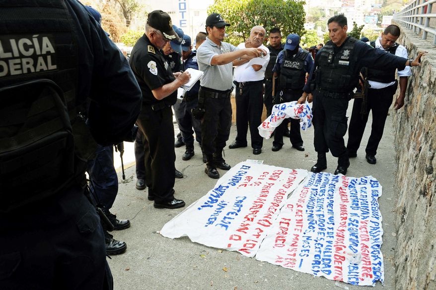 Police examine a &quot;narco-manta,&quot; a warning message painted on a banner left near the site where five dismembered bodies were found on the sidewalk next to a car in Acapulco. (Associated Press)