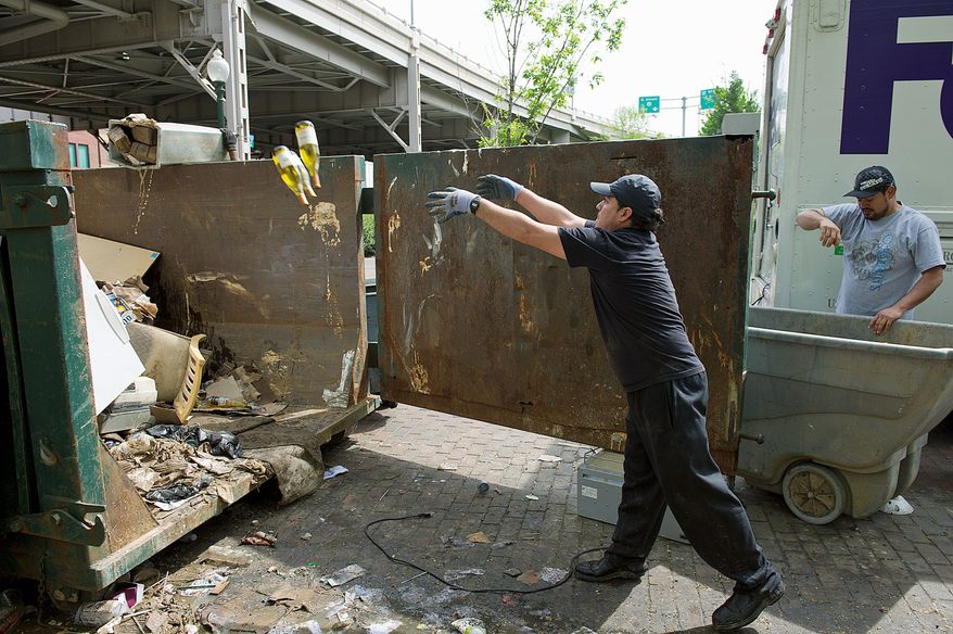 Jesus Gillian (left) and Boly Vasquez, who both work for Cabanas restaurant on the Georgetown waterfront, toss wine bottles into a trash bin Thursday. Water damage from massive flooding earlier in the week forced restaurants to discard food, furniture and more. (Barbara L. Salisbury/The Washington Times)