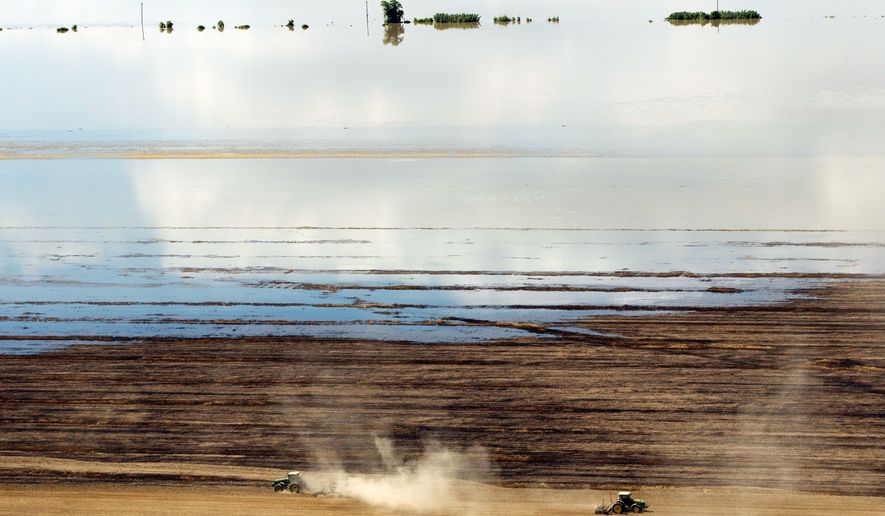 Farmers work as floodwaters from the Mississippi River creep across their fields Tuesday in Natchez, Miss. The Coast Guard said it closed the river at the port in Natchez because barge traffic could increase pressure on levees already burdened by heavy river flow. (Associated Press)