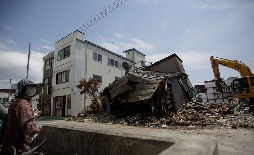 A woman observes the demolition of a house in the northeastern Japanese town of Kesennuma on Friday. Amid the destruction caused by the March 11 tsunami, many of the first shops to reopen have been pubs and grocery stores. (Associated Press)