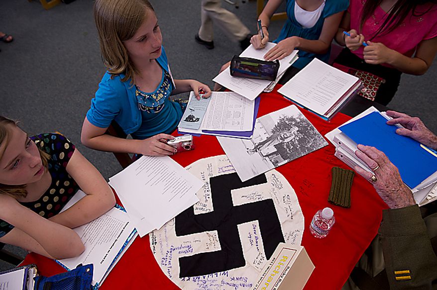 Rocky Run Middle School seventh-graders Alli Bolton, left, and Stephanie Introne, both 12, listen to a World War II vet's stories, including the one about how he captured this Nazi flag, during the school's 10th annual World War II Day, called "The Latest Generation Meets the Greatest Generation," on Thursday, June 9, 2011. The day included small-group interviews with WWII vets as well as panel discussions and World War II-inspired entertainment provided by the students. More than 100 vets participated. (Barbara L. Salisbury/The Washington Times)