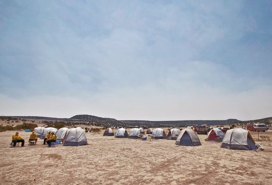 Firefighters in Springerville, Ariz., sit outside tents Wednesday as smoke from the Wallow fire continues to rise nearby. A single campfire is the likely cause of what is now the largest blaze in Arizona history. (Associated Press)