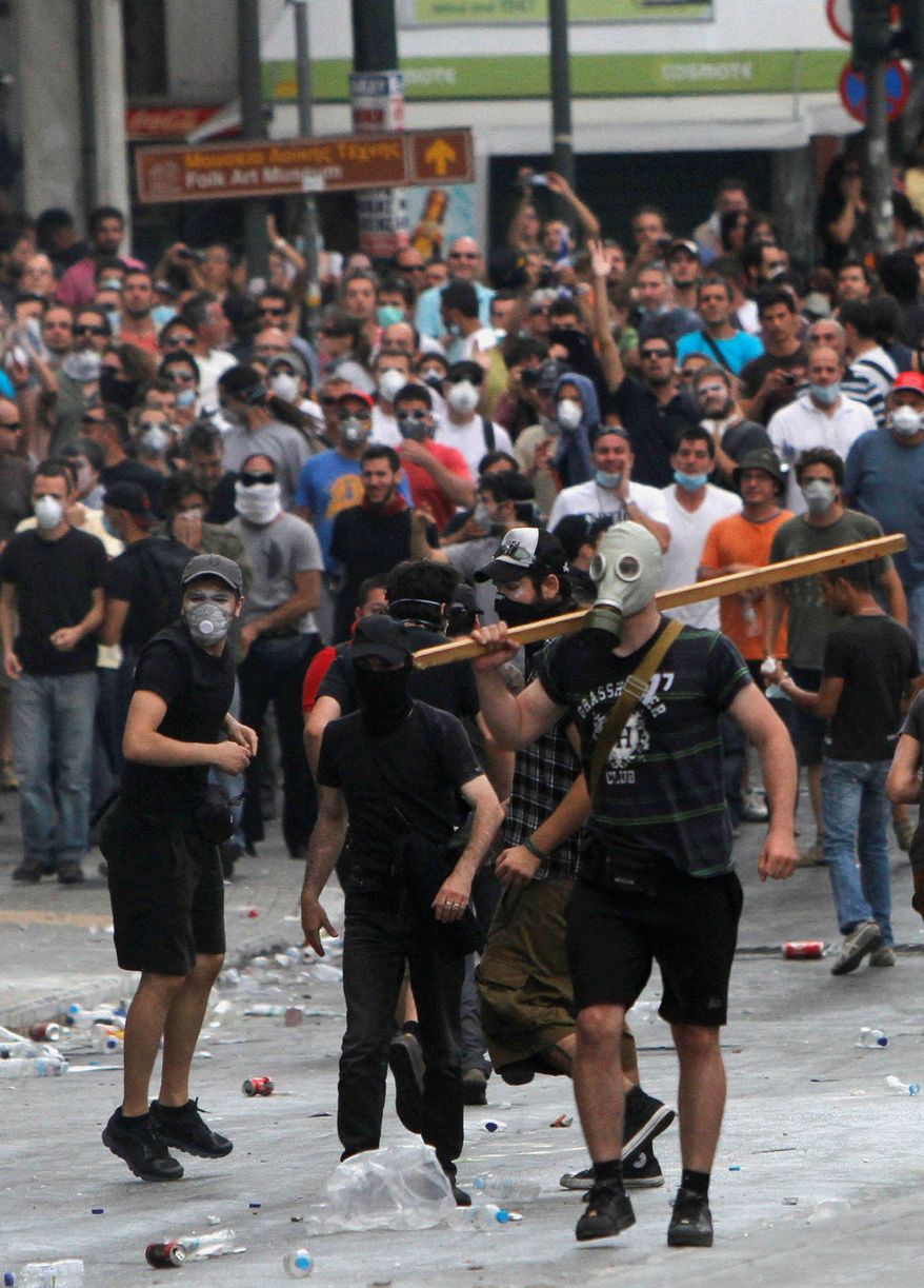 Greek protesters protect themselves with masks and hoods Tuesday as riot police fire volleys of tear gas and stun grenades. (Associated Press)