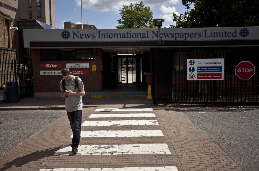 A man looks at a phone in front of a News International building in London on July 6, 2011. (Associated Press)
