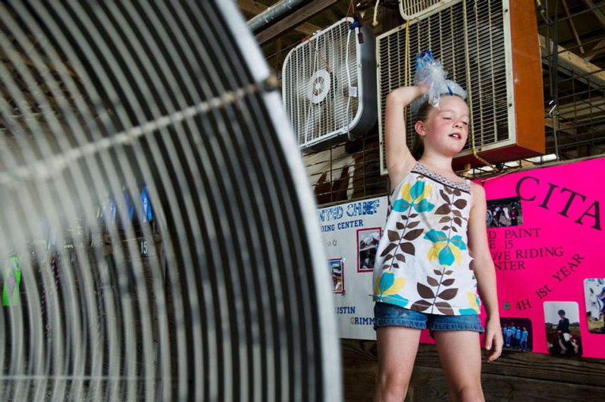 Abigail Gregory, 7, holds an ice bag on her head as she leans up against fans set up in the horse barn at the Bartholomew County 4-H Fair near Columbus, Ind. (AP Photo/The Republic, Alton Strupp)